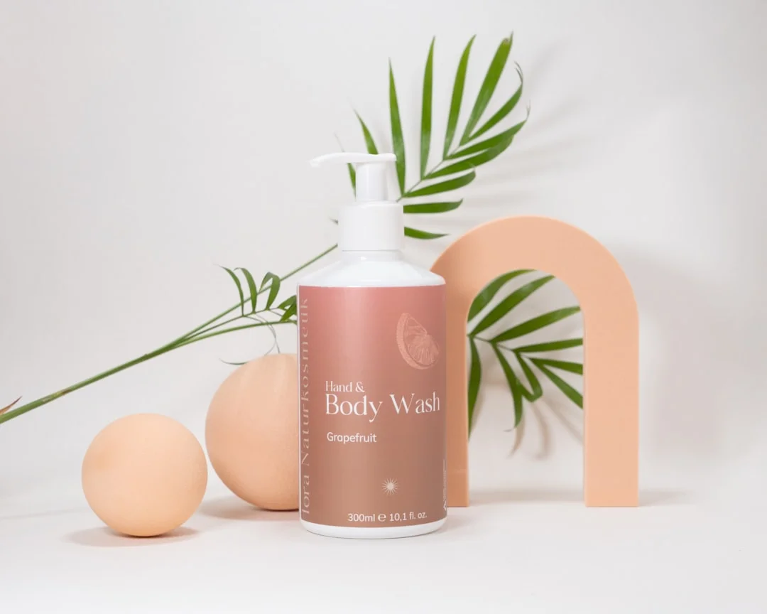 A steamy morning shower scene with a glass shelf holding amber and frosted bottles of natural body wash alongside a wooden bath brush and a sprig of eucalyptus